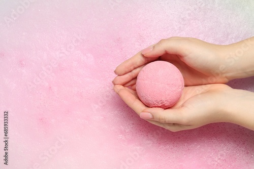 Woman holding bath bomb over water with foam, top view. Space for text