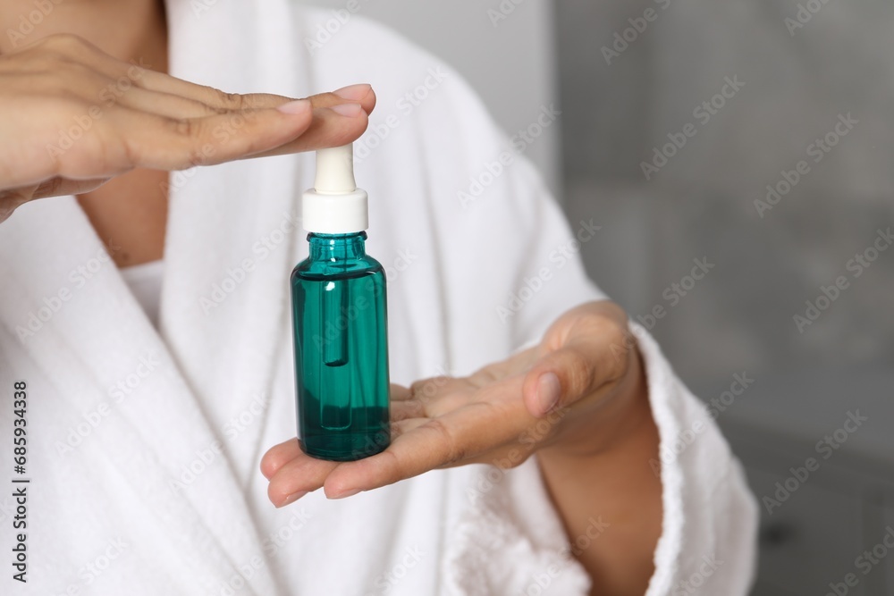 Woman with bottle of cosmetic serum on blurred background, closeup Woman with bottle of cosmetic serum on blurred background, closeup