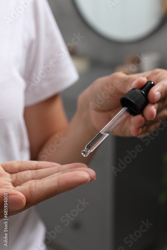 Woman applying cosmetic serum onto her finger on blurred background  closeup