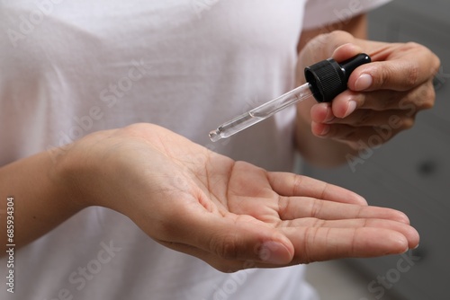 Woman applying cosmetic serum onto her hand on blurred background  closeup