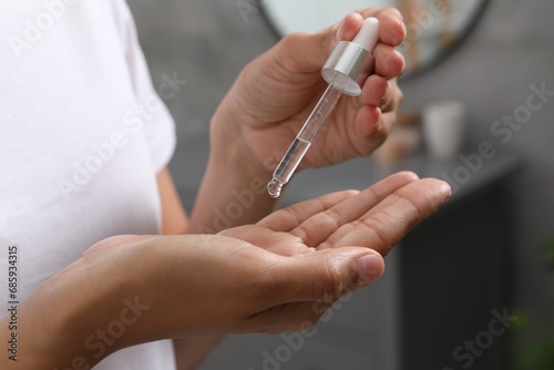 Woman applying cosmetic serum onto her hand indoors  closeup