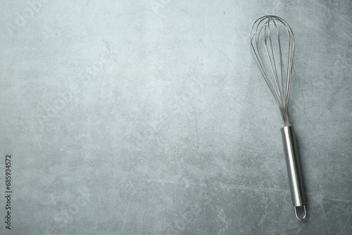 Metal whisk on gray table  top view. Space for text
