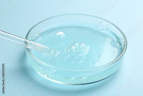 Petri dish with liquid sample and pipette on light blue background, closeup