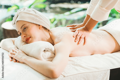 Beautiful young woman received a back massage on a spa bed from professional masseuse. Attractive female relaxes deeply by skilled hands of the massage therapist. Surrounded with nature. Tranquility.