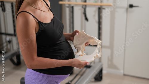 Pregnant woman holding sample of pelvic bones in yoga studio.  photo