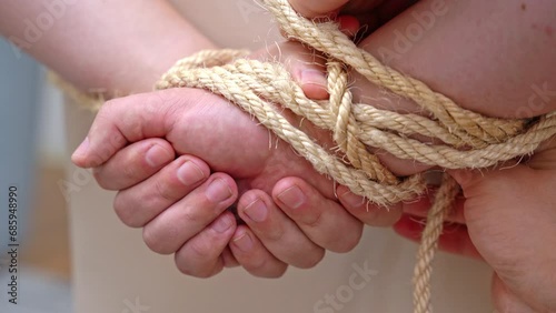 Kidnapper ensures hindrance to escape efforts. Kidnapper binds hands of victim hostage behind back. Hands of victim tied behind back by kidnapper closeup photo
