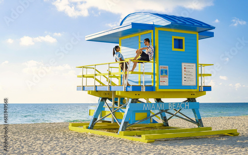 Miami Beach, a couple on the beach in Miami Florida, lifeguard hut Miami Asian women and caucasian men on the beach during sunset. man and woman relaxing at a lifeguard hut looking at a blue ocean