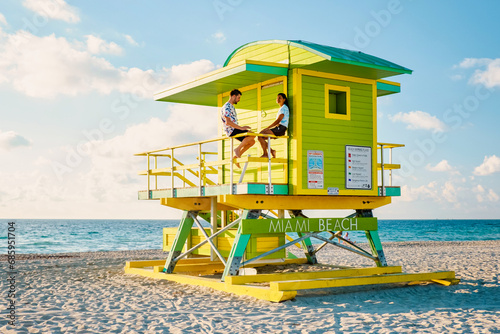 Miami South Beach Florida US, couple by lifeguard hut during sunrise at Miami Beach, men and woman on the beach sitting in a lifeguard hut