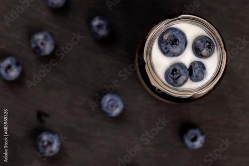 large blueberry berries and yogurt in a glass jar on a black slate board