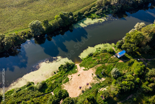 Aerial view of an overgrown river with an empty sandy beach and a lifeguard booth
