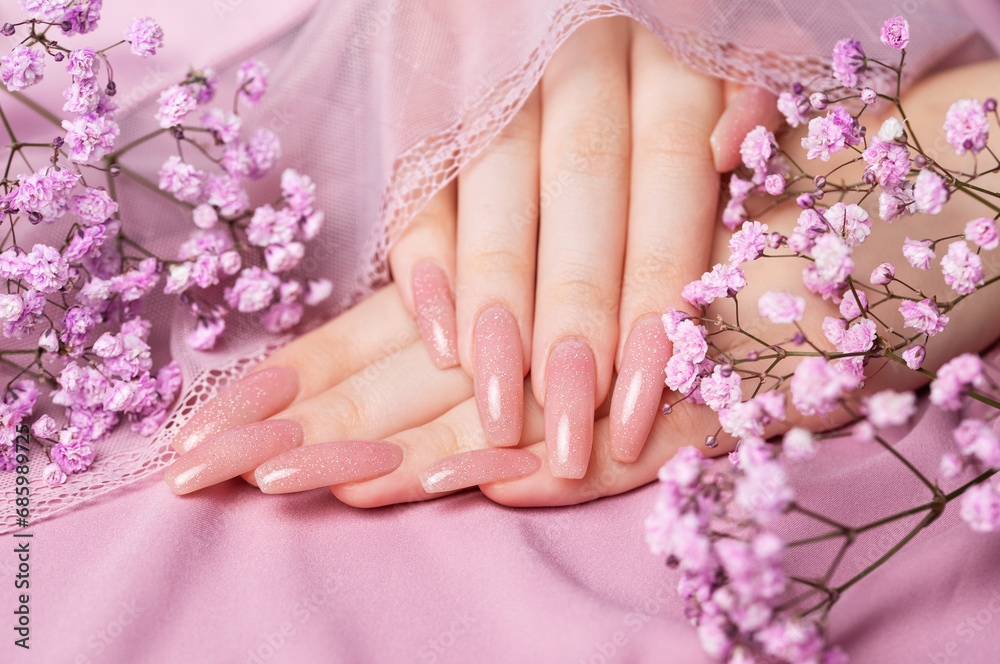 Fototapeta premium Female hands with pink nail design hold gypsophila flowers.