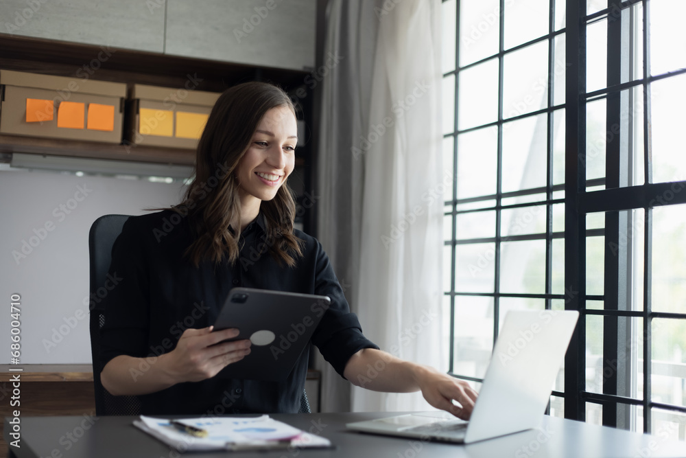 Happy businesswoman using a laptop computer and sitting at desk in office. Happy businesswoman using a laptop computer and sitting at desk in office.
