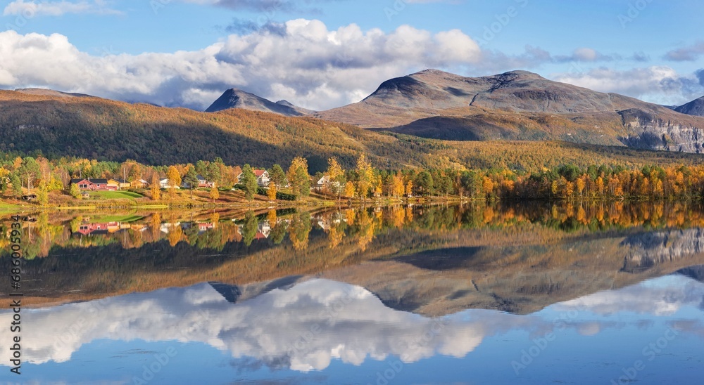 beautiful scenic landscape with mountain and autumnal forest under the sky reflecting in surface of water in Norway.