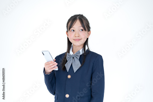 白背景で携帯を触る学生服を着た日本人の女の子