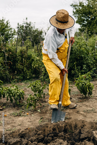 Caucasian farmer hoeing the ground with a shovel.
