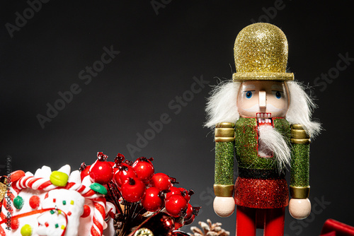 Grandfather Nutcracker stands amidst festive Christmas decorations against a black backdrop. Perfect for holiday banners and seasonal displays.