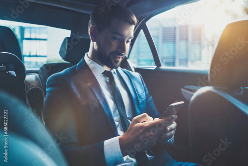 Busy working day. Handsome young man in full suit looking at his smart phone and sitting in the luxury car.Young perfectionist businessman concentrate on the phone.Close-up. © ARVD73