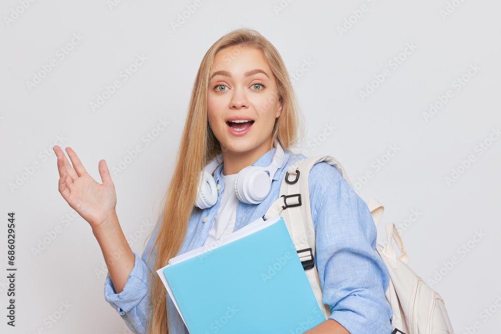 Cheerful blonde student girl with blue folder in hand smiling while posing isolated in studio, good day concept, copy space Cheerful blonde student girl with blue folder in hand smiling while posing isolated in studio, good day concept, copy space