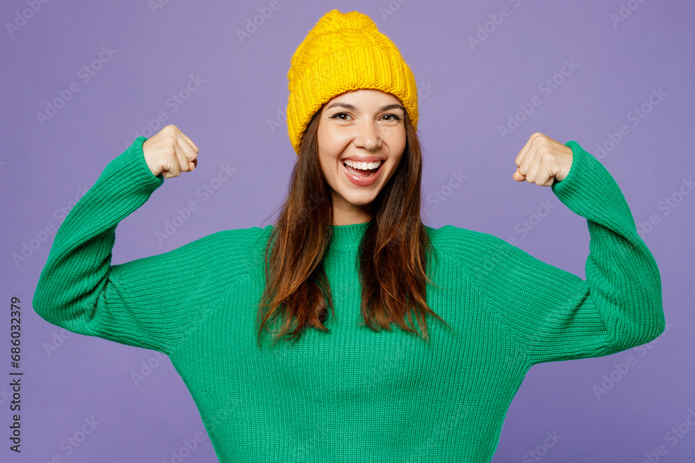 Young woman wear green sweater yellow hat casual clothes showing biceps muscles on hand demonstrating strength power isolated on plain pastel light purple background studio portrait Lifestyle concept Young woman wear green sweater yellow hat casual clothes showing biceps muscles on hand demonstrating strength power isolated on plain pastel light purple background studio portrait Lifestyle concept