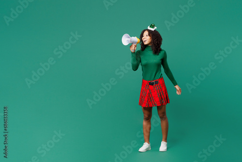 Full body merry little kid teen girl wearing hat casual clothes posing scream in megaphone announces sale isolated on plain green background studio portrait. Happy New Year Christmas holiday concept.
