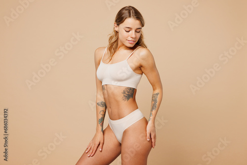 Side profile view young nice lady woman with slim body perfect skin wearing nude top bra lingerie stand puts hand on thigh isolated on plain pastel light beige background Lifestyle diet fit concept.