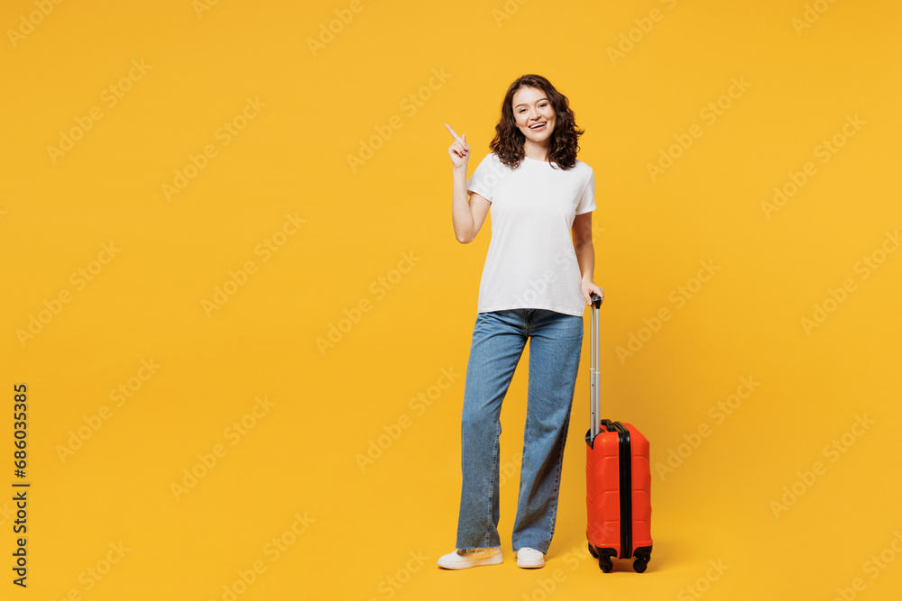 Traveler woman wears t-shirt casual clothes hold suitcase bag point aside isolated on plain yellow background. Tourist travel abroad in free spare time rest getaway. Air flight trip journey concept. Traveler woman wears t-shirt casual clothes hold suitcase bag point aside isolated on plain yellow background. Tourist travel abroad in free spare time rest getaway. Air flight trip journey concept.