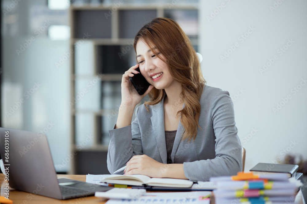 Accounting asian woman use smartphone and laptop at office desk in office, Accounting businesswoman online working concept. Accounting asian woman use smartphone and laptop at office desk in office, Accounting businesswoman online working concept.