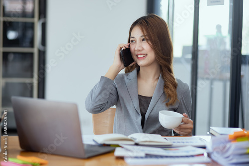 Accounting asian woman use smartphone and laptop at office desk in office, Accounting businesswoman online working concept.