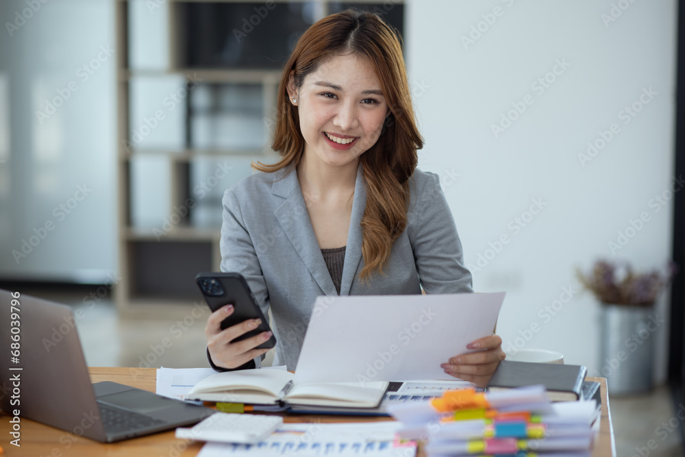 Accounting asian woman use smartphone and laptop at office desk in office, Accounting businesswoman online working concept. Accounting asian woman use smartphone and laptop at office desk in office, Accounting businesswoman online working concept.