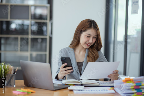 Accounting asian woman use smartphone and laptop at office desk in office, Accounting businesswoman online working concept. © SOMKID