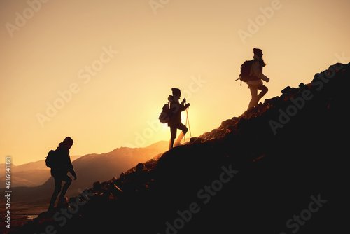 Group of hikers with backpacks walks uphill in sunset mountains