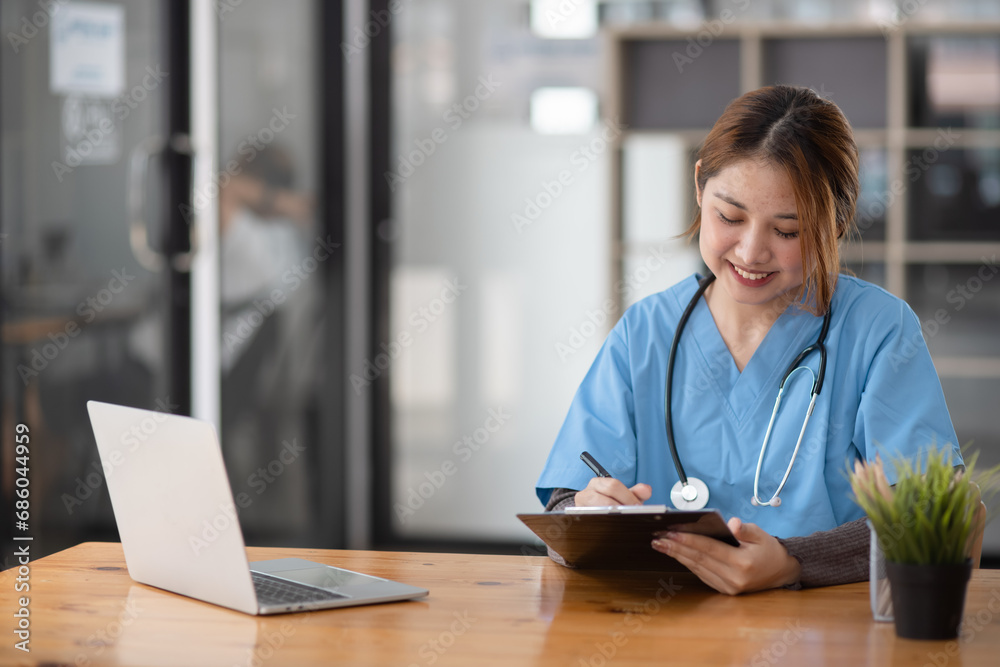 Asian female doctor working with a patient clipboard and digital laptop sitting at desk in hospital, Medicine and healthcare concept. Asian female doctor working with a patient clipboard and digital laptop sitting at desk in hospital, Medicine and healthcare concept.
