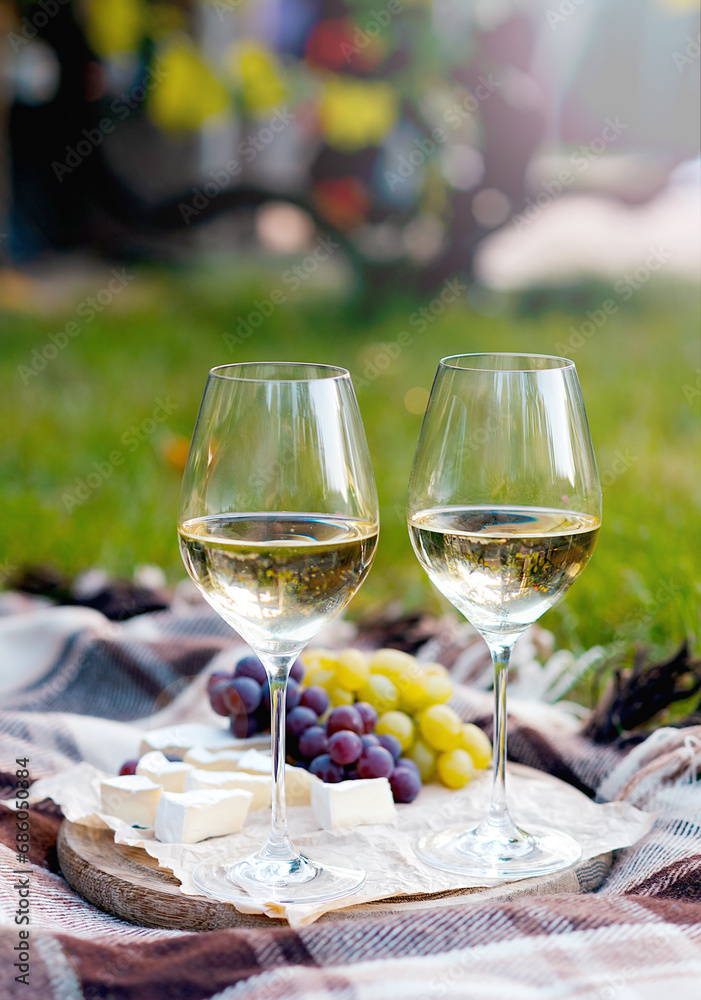 Two glasses of white wine and a wooden plate with cheese and grapes served outside