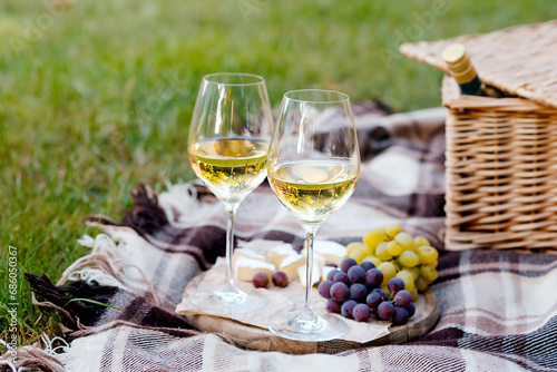 Two glasses of white wine and a wooden plate with cheese and grapes served outside