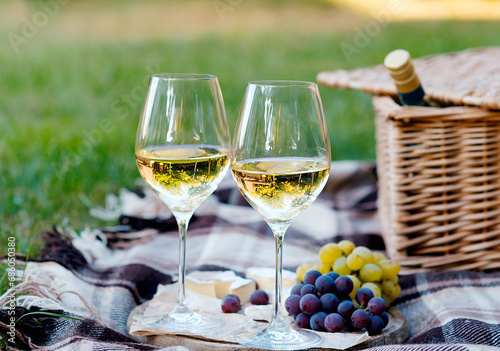 Two glasses of white wine and a wooden plate with cheese and grapes served outside