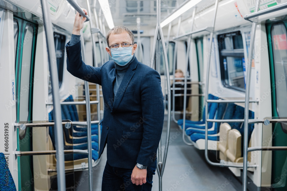 Businessman commuting on a subway train, holding onto a handle, wearing a face mask Businessman commuting on a subway train, holding onto a handle, wearing a face mask