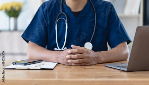 Asian male doctor with patient clipboard and laptop computer sitting at desk in hospital, Medicine and healthcare concept.