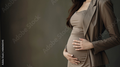 A pregnant woman holds her belly against a dark background