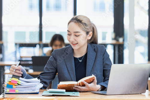 Asian businesswoman working on laptop and financial document paper sitting at desk in office workplace.