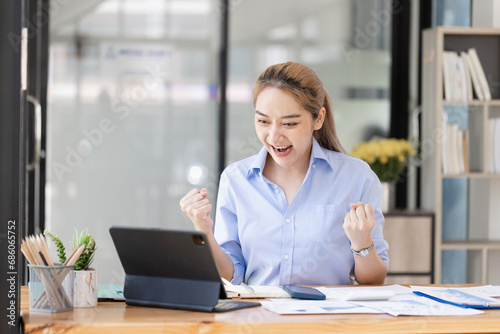 Happy excited young Asian woman winner and celebrating success at desk in office.
