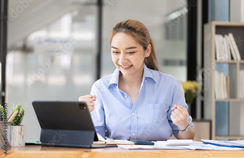 Happy excited young Asian woman winner and celebrating success at desk in office.