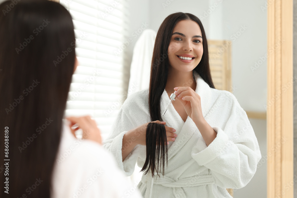 Beautiful woman applying hair serum indoors, reflection in mirror. Cosmetic product Beautiful woman applying hair serum indoors, reflection in mirror. Cosmetic product