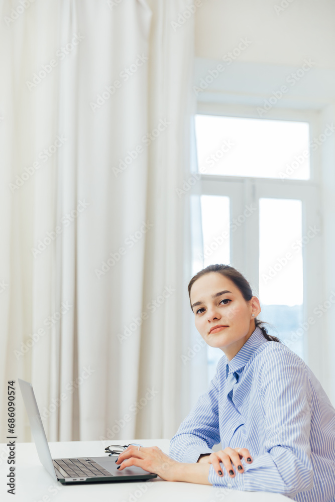Image of young pleased happy cheerful cute beautiful business woman sit indoors in office using laptop Image of young pleased happy cheerful cute beautiful business woman sit indoors in office using laptop