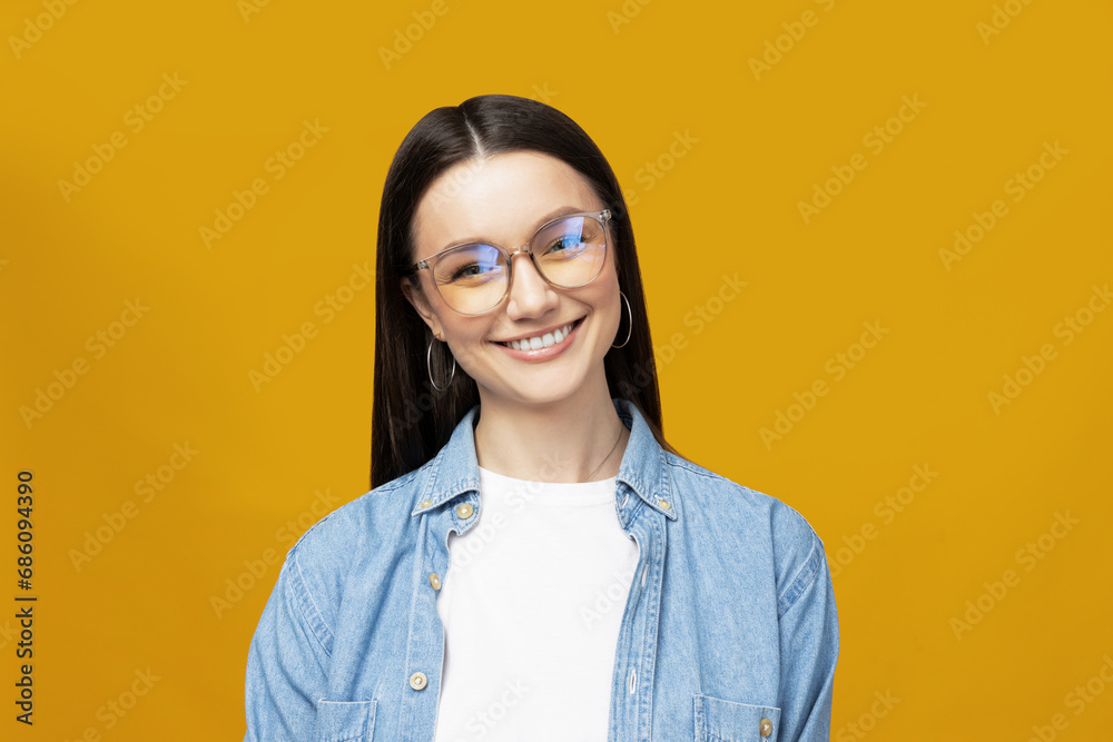 A beautiful girl in glasses poses on a yellow background
