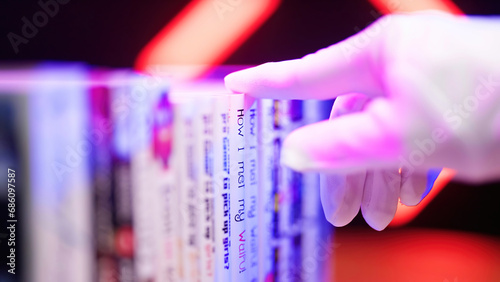 Hand in gloves pick Japanese manga comics from a bookshelf with neon lights in background