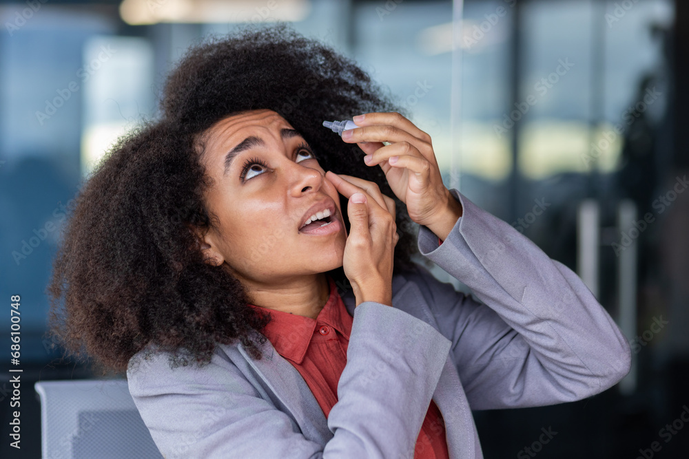 Business woman drips eye drops, businesswoman working long time with laptop, overworked and tired at workplace inside office, worker in business suit and curly hair Business woman drips eye drops, businesswoman working long time with laptop, overworked and tired at workplace inside office, worker in business suit and curly hair