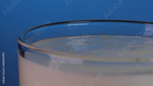 Extreme close up glass of yogurt,  strawberries and blueberries fall in it on a blue background. Slow motion 200 fps