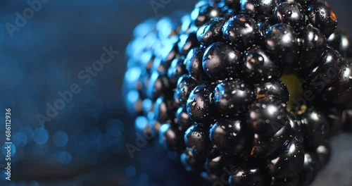 Extreme close up  of one fresh ripe blackberry rotating  on a black plate on a blue background with drops of water
