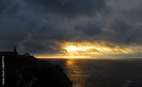 Cloudy and golden sunset at Cape San Vicente with the silhouette of the lighthouse on the cliffs. Cape Saint Vincent is in Algarve, Portugal, the most extreme geographical point in southwestern Europe