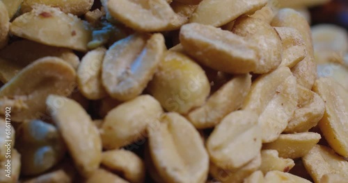 Extreme close up fried peanuts rotate on a black plate on a blue background.